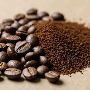 Puede incluir: Primer plano de granos de café tostados y café molido. Los granos de color marrón oscuro están enteros y dispersos, con un montón de café finamente molido a la derecha. La imagen está tomada sobre un fondo neutro, resaltando las texturas y colores del café.
