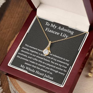 May include: A gold-tone pendant necklace with a central round clear stone, presented in a dark wooden box. The box insert features the text: To My Adoring Fiancee Lily, followed by a message about a shared journey and the signature My Whole Heart Julian.