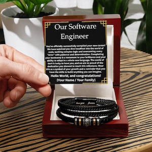 May include: A black leather bracelet with silver and gold accents, presented in a wooden box. The box contains a message for a software engineer. The bracelet has the words "love you forever" engraved on it.