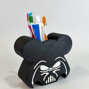 Peut inclure: Porte-brosse à dents noir sur le thème de Dark Vador avec un motif de visage blanc. Le support a la forme d'oreilles de Mickey Mouse. Il contient une brosse à dents rose et verte, une brosse à dents orange et un tube de dentifrice.