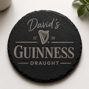 May include: A round, black slate coaster with the name "David's" in cursive script. Below, the Guinness logo is displayed with the text "GUINNESS DRAUGHT" and the numbers "17" and "59". The coaster has a rough, natural edge.