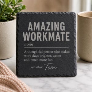 Könnte beinhalten: Ein quadratischer Untersetzer aus schwarzem Schiefer mit rauen, gemeißelten Kanten. Der hellgrau eingravierte Text lautet: AMAZING WORKMATE noun A thoughtful person who makes work days brighter, easier and much more fun. see also: Tom.