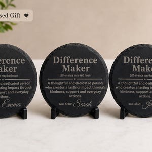 以下が含まれることがあります： 「Difference Maker」の文字と定義が書かれた黒いスレートコースター3枚。各コースターにはEmma、Sarah、Jamesと異なる名前が書かれています。コースターは黒いスタンドに置かれています。