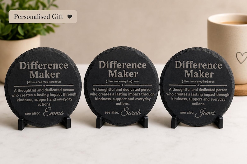 以下が含まれることがあります： 「Difference Maker」の文字と定義が書かれた黒いスレートコースター3枚。各コースターにはEmma、Sarah、Jamesと異なる名前が書かれています。コースターは黒いスタンドに置かれています。