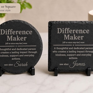以下が含まれることがあります： 「Difference Maker」の文字と定義が書かれた、丸と四角の黒いスレートコースター2つ。丸いコースターには「see also: Sarah」、四角いコースターには「see also: James」と書かれています。どちらも黒いスタンドに置かれています。