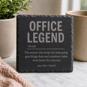 Könnte beinhalten: Ein quadratischer Untersetzer aus schwarzem Schiefer mit rauen, natürlichen Kanten. Der Text lautet: OFFICE LEGEND noun. The person who keeps the team going, gets things done and somehow makes work better for everyone. see also: Sarah. Die Schrift ist hellgrau.