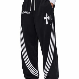 May include: Black sweatpants with white accents and a cross graphic. The pants feature three white stripes down the side and the text "Night Raid" in white. The pants have a drawstring waist.