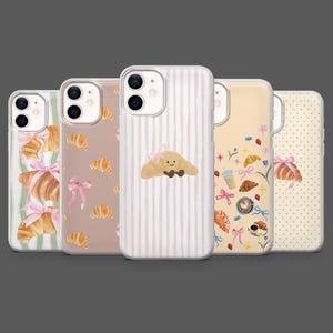 Può includere: Una collezione di cinque custodie per telefono con vari disegni. Le custodie presentano illustrazioni di croissant, fiocchi e caffè. I colori includono rosa, beige e bianco. Alcune custodie hanno motivi a righe o a pois.