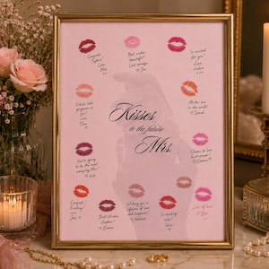 Könnte beinhalten: Gerahmter rosa Druck mit Lippenstift-Kussspuren und handgeschriebenen Nachrichten. Der Text "Kisses to the future Mrs." ist in eleganter Schrift. Der goldene Rahmen umgibt den Druck, passend für eine Hochzeit.