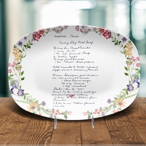 May include: Oval white serving platter with a floral border and handwritten recipe text. The recipe is for "Every Day Meat Loaf" and includes ingredients like ground beef and bread crumbs. The platter is displayed on a wooden surface.