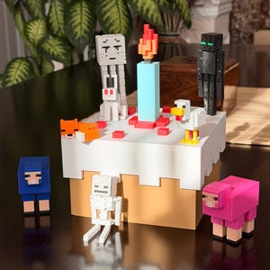 Pode incluir: Um bolo de aniversário com tema Minecraft com várias figuras de personagens. O bolo apresenta uma vela azul com uma chama vermelha e laranja, e é cercado por figuras como um esqueleto, uma ovelha e um Enderman. O bolo é branco com uma base bege.