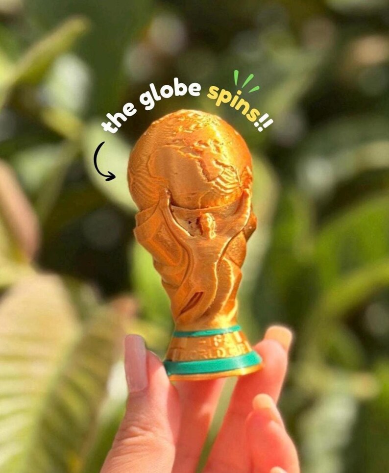 May include: A gold-colored trophy with a globe design, featuring a green base. The text "the globe spins!!" is written above the trophy. The trophy is held by a person.