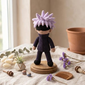 May include: A crocheted doll featuring spiky light purple hair, a black blindfold over the eyes, and a dark purple high-collar jacket with matching pants. The doll stands on a circular wooden base, showcasing detailed yarn work and a neutral skin tone.