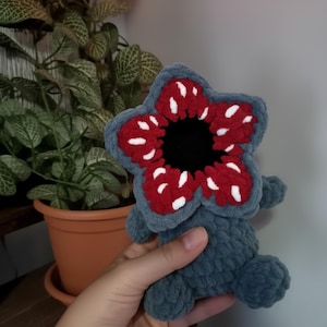 May include: A handmade Demogorgon plush toy in grey, red, white, and black. The creature features a large, flower-like head with red petals dotted with white spots, a black centre, and a grey body.