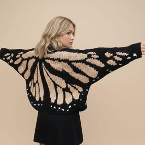 May include: A black knit sweater with a butterfly wing design in tan and white. The sweater has a round neckline and long sleeves. The butterfly wing design covers the back and extends to the sleeves, creating a unique and eye-catching look.