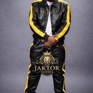 K&ouml;nnte beinhalten: Schwarzes Lederjacken- und Hosen-Set mit gelben Streifen. Die Jacke hat eine Knopfleiste und die Hose ein Logo am Bein. Das Set ist von Jaktor Leather.