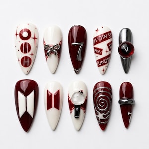 May include: A set of ten press-on nails in a pointed almond shape, featuring a color palette of deep burgundy, white, and metallic silver. Designs include the text OOH, a silver bow, the number 7, names, a V-sphere, logos, and a star swirl.
