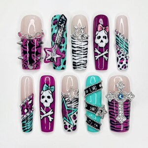 May include: A set of ten long, rectangular press-on nails featuring a variety of designs including purple and teal animal prints, black and white zebra stripes, skull and crossbones motifs, a 3D guitar charm, silver studs, and a large cross.