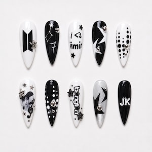 May include: A set of ten stiletto-shaped press-on nails in black and white. Designs include the BTS logo, the text i <3 jimin, bangtan, and JK, a portrait of a person, musical notes, stars, constellations, and polka dots with silver studs.