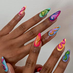 May include: A close-up of a hand with long, almond-shaped nails. Each nail is painted a different bright color, including pink, yellow, blue, and green, with abstract swirled designs in contrasting colors. The nails have a glossy finish.