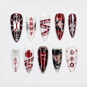 May include: A set of ten almond-shaped press-on nails featuring a red and white color palette. Designs include the BTS logo, the word ARMY, member names, portraits, a red rose, the text WHAT IS YOUR LOVE SONG, the number 7, and silver accents.