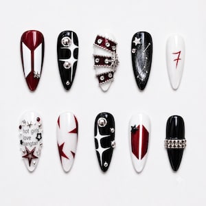 May include: A set of ten almond-shaped press-on nails featuring a black, white, and deep red color palette. Designs include star motifs, silver studs, a constellation pattern, the number 7, and the text hot girls love bangtan with star charms.