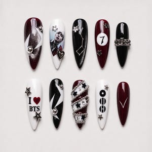 May include: A set of ten stiletto-shaped press-on nails featuring a color palette of black, white, and deep red. Designs include a portrait, the number 7, star charms, silver studs, a heart charm, the text I love BTS, and a V-shaped accent.