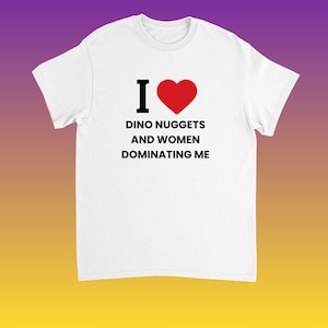 May include: White t-shirt with the text "I ♥ Dino Nuggets and Women Dominating Me" in black font, with a red heart symbol. The shirt has short sleeves and a crew neck.
