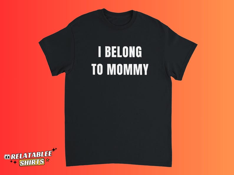May include: Black t-shirt with the white text "I BELONG TO MOMMY". The shirt has short sleeves and a crew neck. The text is centered on the front of the shirt. The background is a gradient of orange and red.