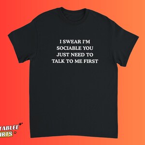 May include: Black t-shirt with the text "I SWEAR I'M SOCIABLE YOU JUST NEED TO TALK TO ME FIRST" in white. The shirt has short sleeves and a crew neck. The brand logo "RELATABLEE SHIRTS" is in the bottom left corner.