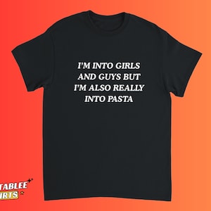 以下が含まれることがあります： 「I'M INTO GIRLS AND GUYS BUT I'M ALSO REALLY INTO PASTA」と白い文字で書かれた黒いTシャツ。Tシャツは半袖で丸首です。背景はオレンジと赤のグラデーションです。
