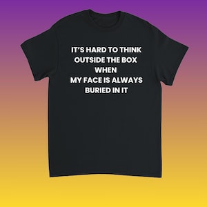 Może przedstawiać: Czarny t-shirt z białym tekstem: "IT'S HARD TO THINK OUTSIDE THE BOX WHEN MY FACE IS ALWAYS BURIED IN IT." Koszulka jest prezentowana na fioletowo-żółtym tle gradientowym.