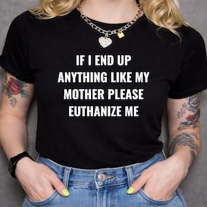 Könnte beinhalten: Ein schwarzes kurzärmeliges T-Shirt mit dem weißen Aufdruck IF I END UP ANYTHING LIKE MY MOTHER PLEASE EUTHANIZE ME. Das Shirt wird mit einer blauen Jeans und einer silberfarbenen Gliederkette mit herzförmigem Anhänger kombiniert.