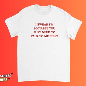 May include: White t-shirt with the text "I SWEAR I'M SOCIABLE YOU JUST NEED TO TALK TO ME FIRST" in red. The shirt has a crew neck and short sleeves. The Relatablee Shirts logo is at the bottom left.