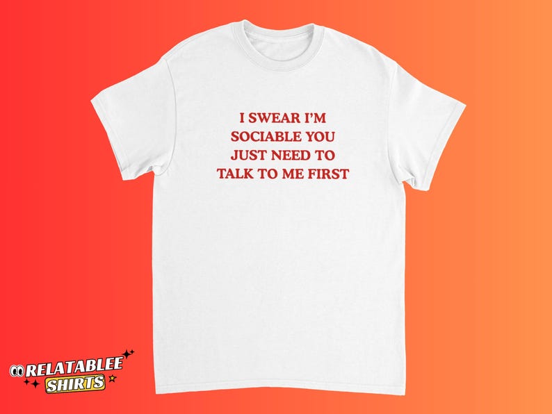 May include: White t-shirt with the text "I SWEAR I'M SOCIABLE YOU JUST NEED TO TALK TO ME FIRST" in red. The shirt has a crew neck and short sleeves. The Relatablee Shirts logo is at the bottom left.