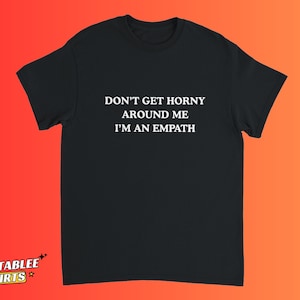 May include: Black t-shirt with the text "DON'T GET HORNY AROUND ME I'M AN EMPATH" in white. The shirt is displayed against a gradient orange and red background. The Relatablee Shirts logo is in the bottom left corner.