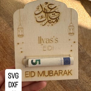 Può includere: Porta regalo in legno Eid Mubarak con calligrafia araba incisa e il nome "Ilyas's". Presenta una fessura per il denaro e il testo "EIDI". Include una banconota da 5 euro. Include anche il testo "SVG DXF AI CUT FILE".