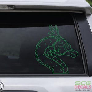 May include: A green outline of a dragon's head and body, a decal, is displayed on a car window. The dragon is facing right, with detailed features. The decal is a vibrant green color.
