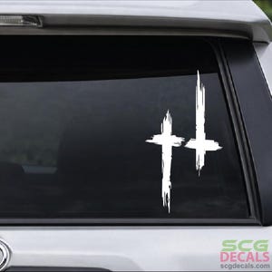 May include: White, distressed cross decal on a vehicle window. The decal features two crosses with a textured, brushstroke effect. The decal is applied to the rear window of a vehicle. The bottom right corner of the image shows the text "SCG DECALS".