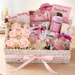 Könnte beinhalten: Ein Geschenk-Korb gefüllt mit rosa Rosen, Schönheitsprodukten und einer dekorativen Schleife. Der Korb enthält Artikel der Marke ISANA, eine Gesichtsmaske und ein Banner mit der Aufschrift "Happy Birthday". Der Korb ist mit einem Blumenmuster verziert.