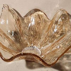 May include: A clear glass bowl with a flower-like shape and a textured surface. The bowl is a light amber color.