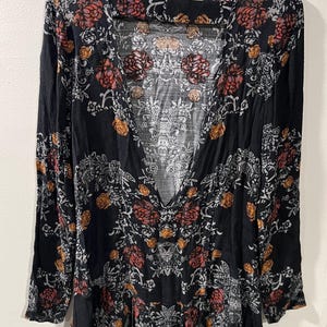 May include: A black long-sleeved dress with a floral print in shades of red, orange, and white. The dress has a deep V-neckline and a ruffled hem.