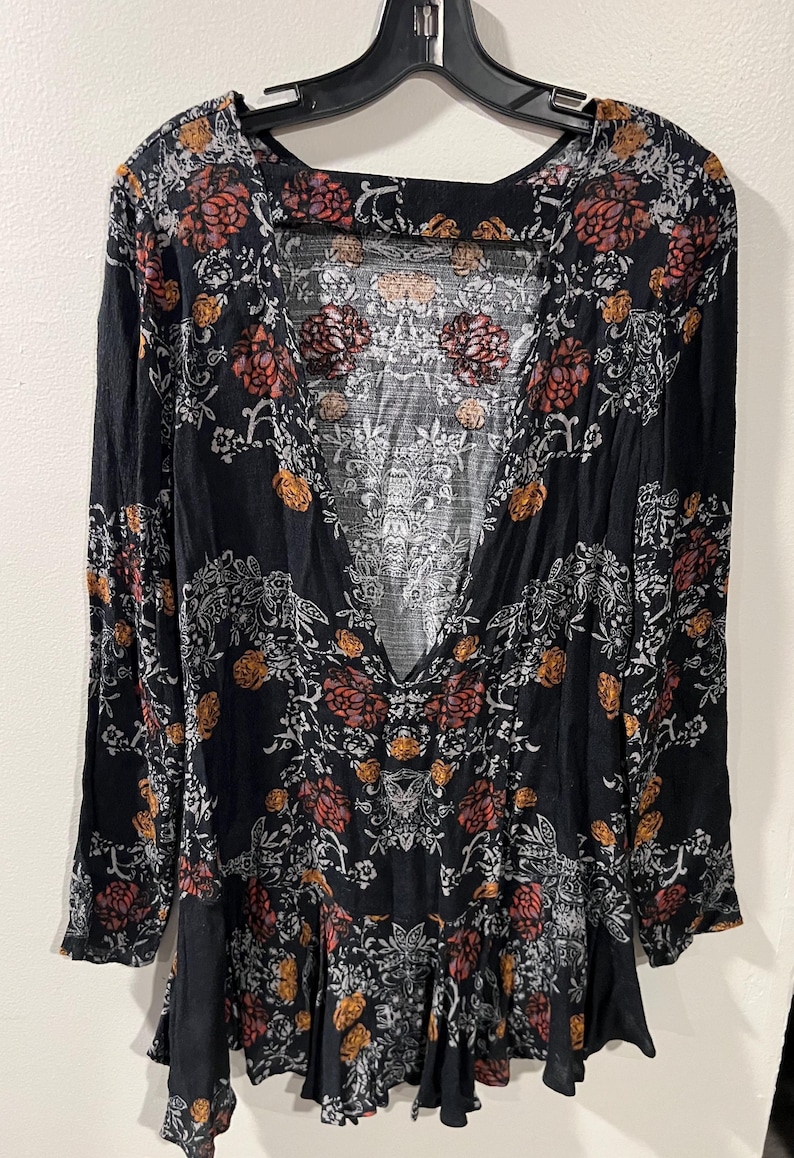 May include: A black long-sleeved dress with a floral print in shades of red, orange, and white. The dress has a deep V-neckline and a ruffled hem.