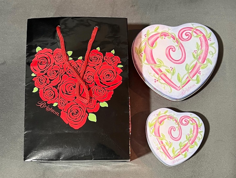 May include: A black gift bag with a red rose heart design and the word "Brighton". Two heart-shaped tins with pink heart designs and green vines. The tins have the word "Brighton" on them.