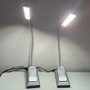 May include: Two silver flexible-neck desk lamps with white LED lights. The lamps have a rectangular base with a switch on the side.