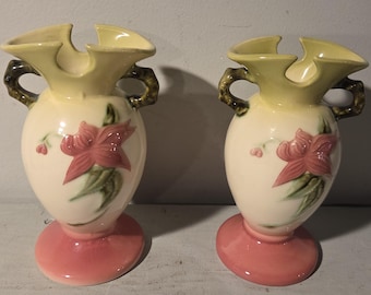 May include: Two vintage ceramic vases with a yellow glaze and pink floral designs. The vases have a unique shape with a flared top and two handles.