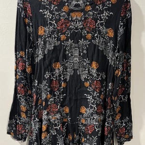 May include: A black long-sleeved dress with a floral print in shades of white, orange, and red. The dress has a round neckline and a flowing skirt.