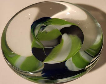May include: A clear glass paperweight with a swirling design of green, white, and blue.