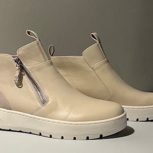 May include: A pair of beige leather ankle boots with a side zipper and a white platform sole.