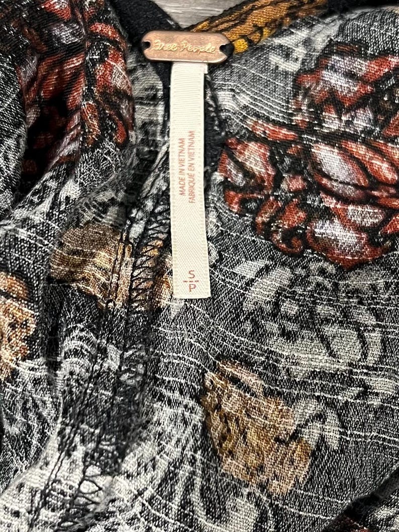 May include: A black and white floral print fabric with a Free People tag attached. The tag is white with black text that reads "Free People" and "Made in Vietnam / Fabrique en Vietnam".